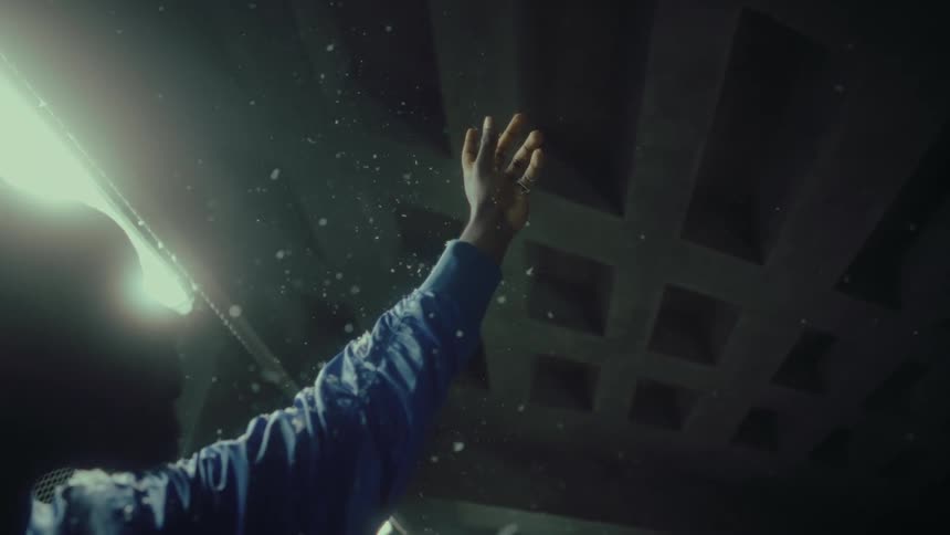 White confetti falls over a young man standing inside a tunnel with his hand raised to the ceiling