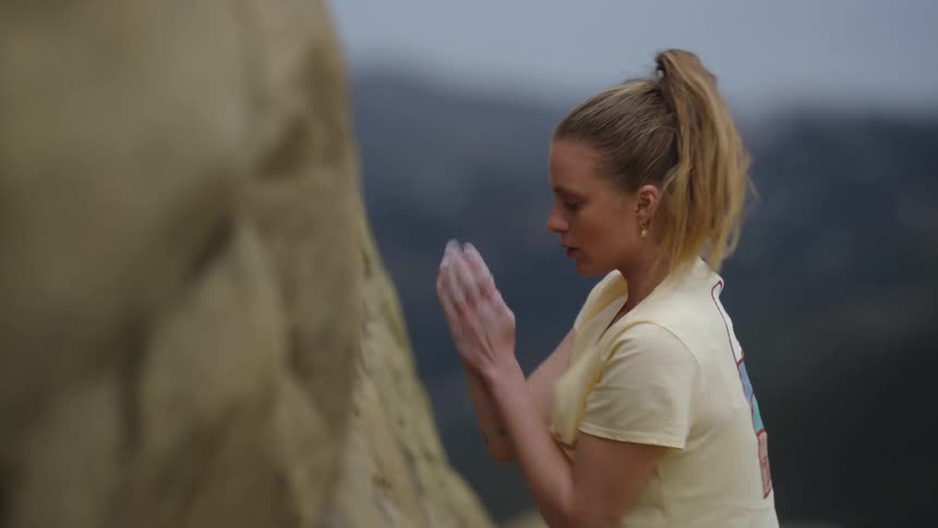A rock climber rubs chalk on her hands before a climb