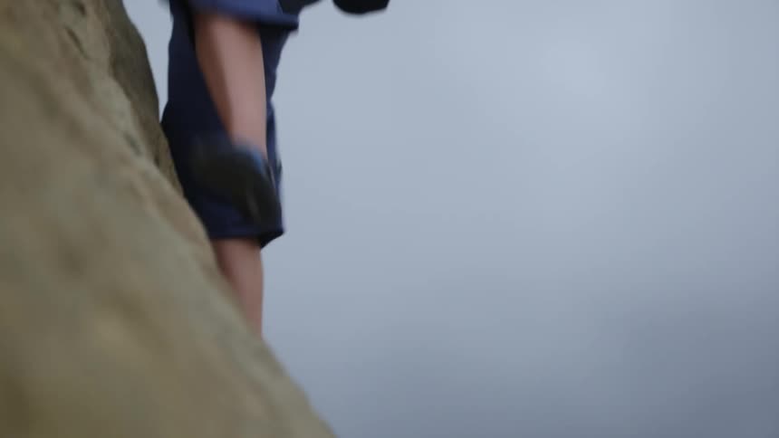 Young woman pushes herself up while climbing a rock wall on a mountain