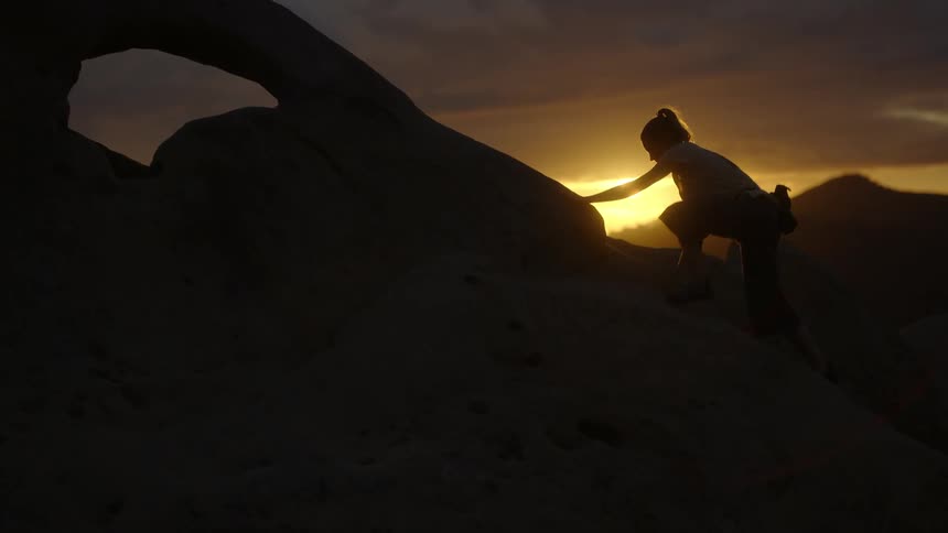 A woman climbing rocks in nature at sunset