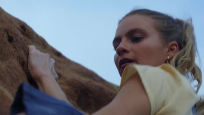 A woman uses her strength to pull herself of a cliff while shes rock climbing