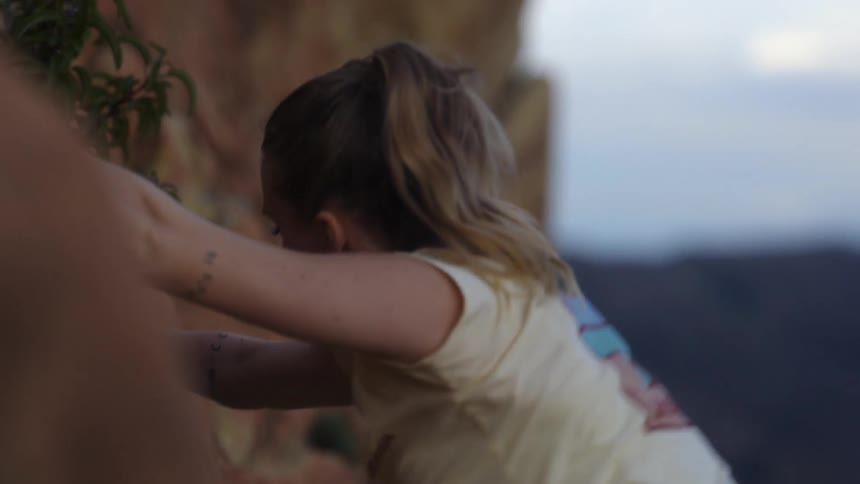 A woman is climbing the side of a mountain and holding on to rocks as she pulls herself up