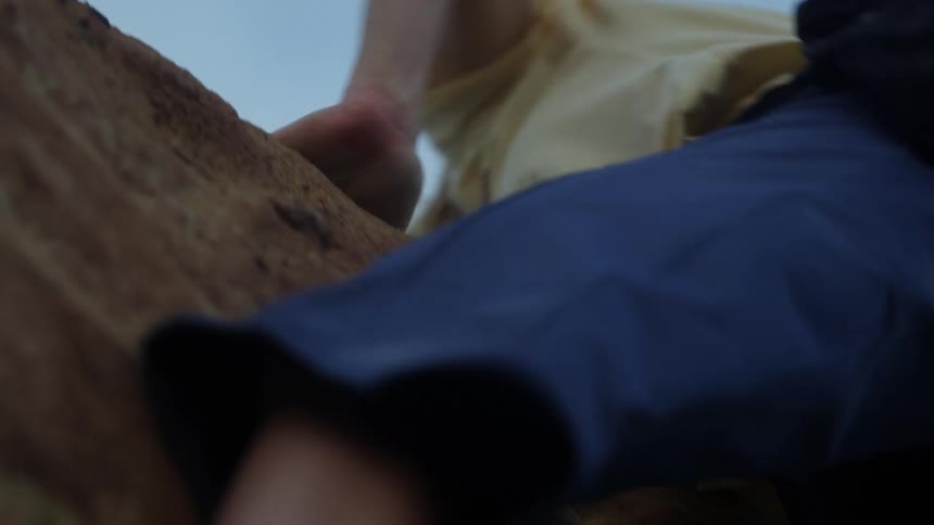 A determined woman pulls herself up while scaling a cliff while rock climbing