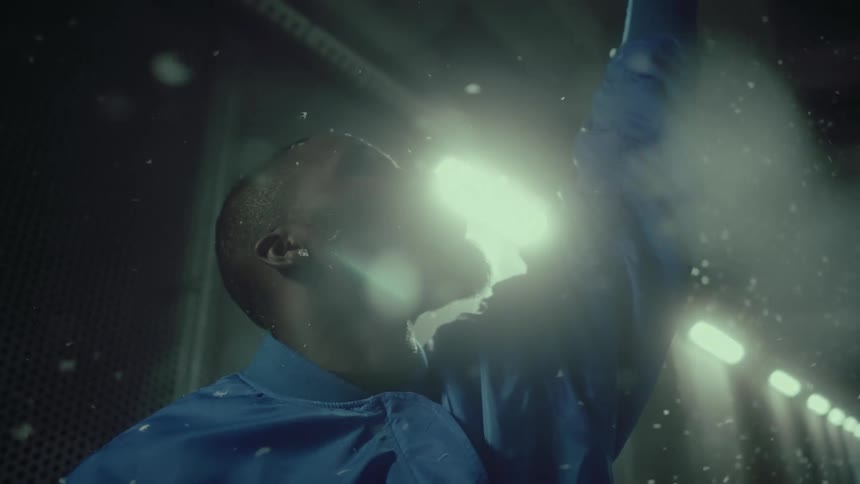 White confetti falls over a young man standing inside a tunnel with his hand raised to the ceiling