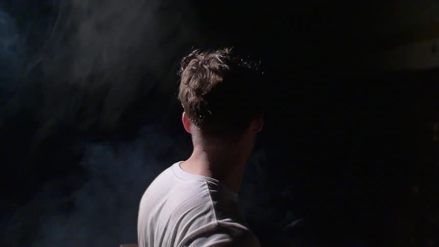 A man stands in a dark area with smoke behind him