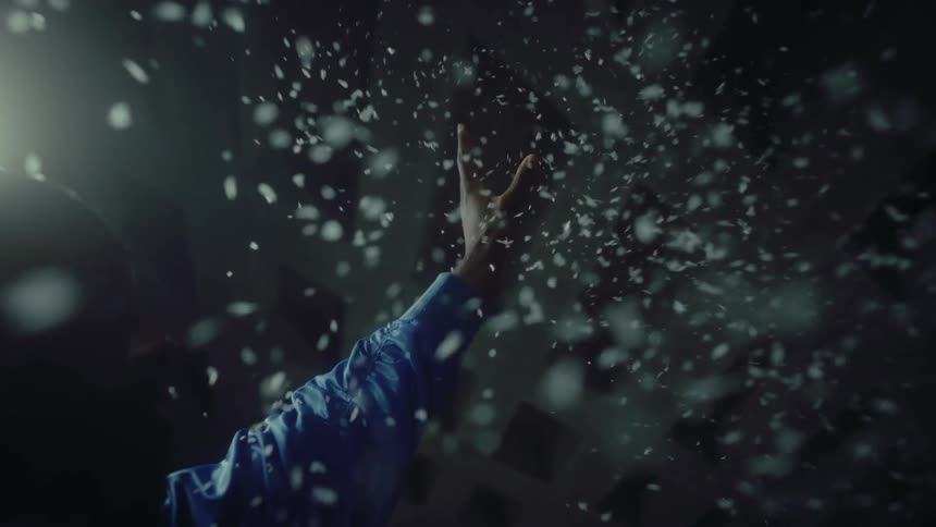 Black man releases white confetti while standing under a white light in a building