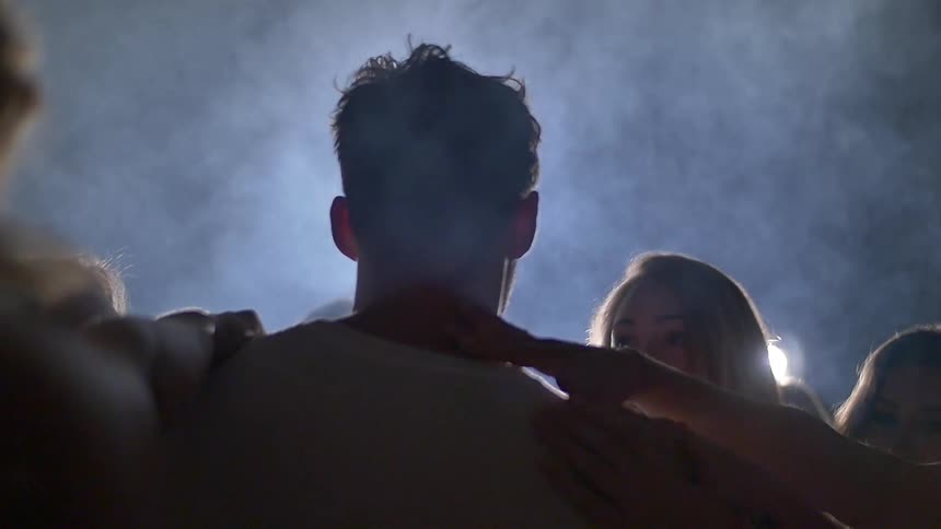 A man walks through a smokey room as women reach out to touch him
