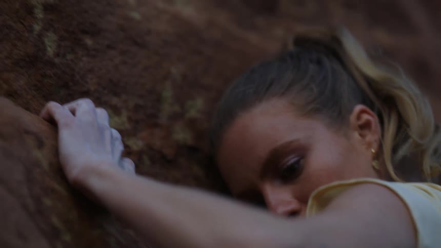 Young blonde woman pushes herself up while climbing a rock wall on a mountain