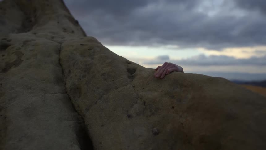 Woman uses her hand to grip the edge of a rock while climbing