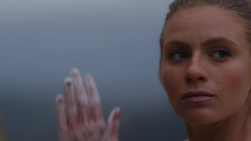 Blonde woman rubs white powder on her hands while mountains and a village sit in the distance