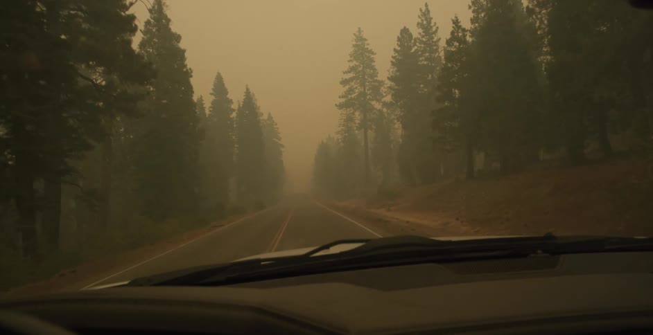 A vehicle drives a long a road through a forest that is hazy due to smoke from a forest fire