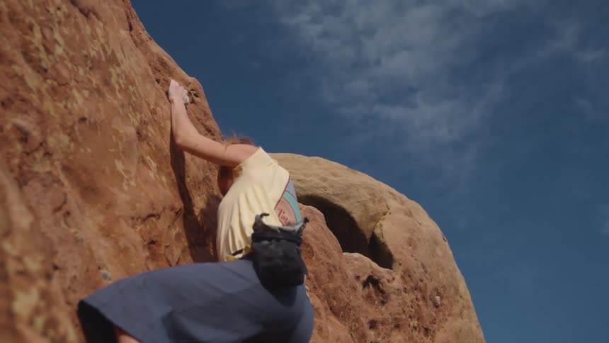Woman climbs bare rock wall under a lightly clouded sky