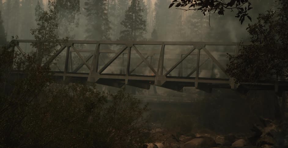 A bridge in a forest with flames rising and smoke filling the air