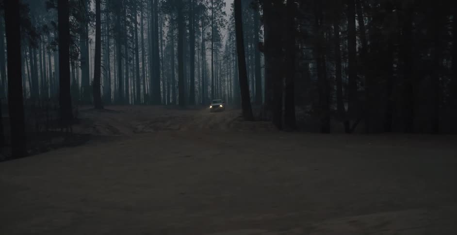 An automobile with the headlights on is traveling on a winding road through a smoke filled forest