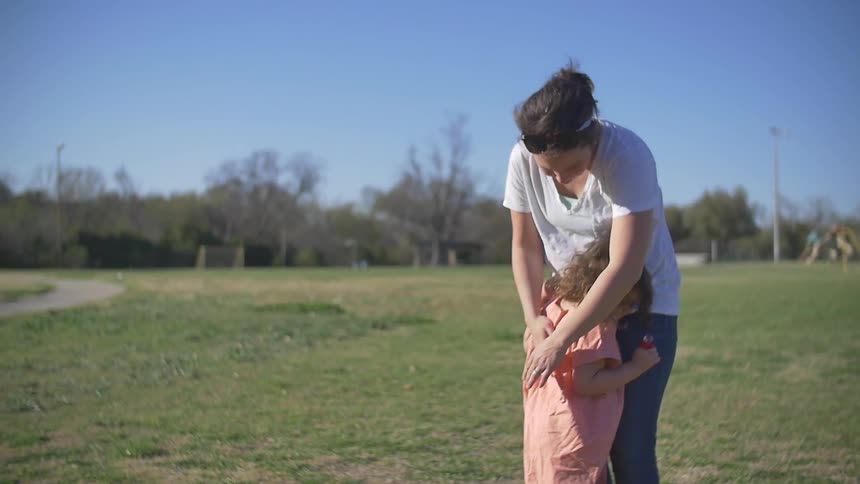 A woman rubs the back of a child leaning against her