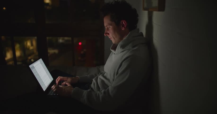 A man sitting with his laptop looks up to think as a vehicle drives by along the street below