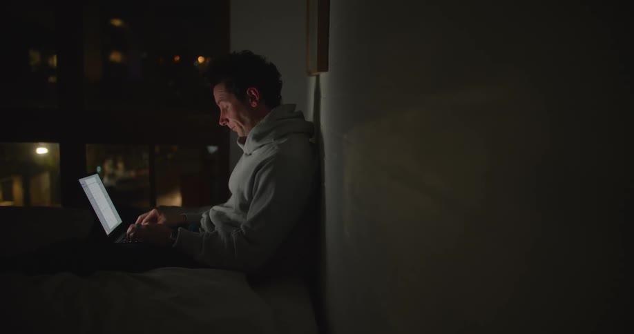 Young tired man yawns while working at home on a laptop at night