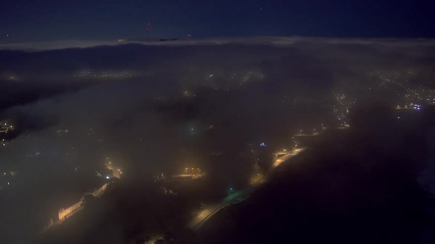 A layer of clouds hanging over highway and city lights clearing at a lit baseball field