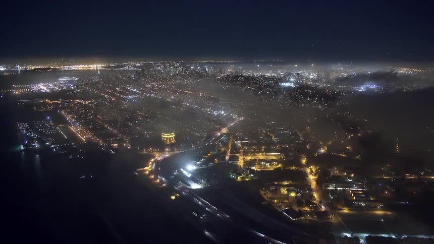 A city is lit up at night and headlights can be seen moving on a highway