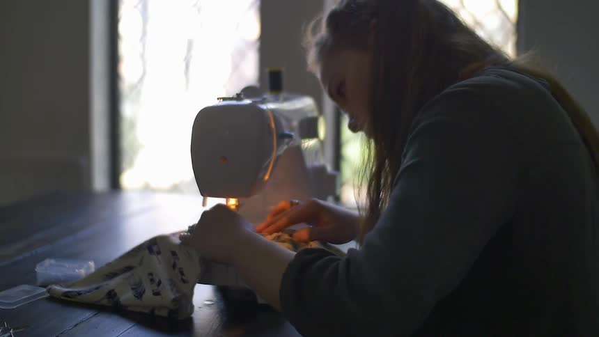 A woman guiding a piece of fabric through a sewing machine