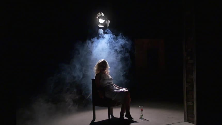 A woman sitting under a stage light as smoke swirls around her