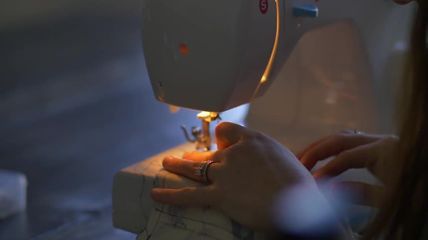A woman uses a sewing machine in a dimly lit space