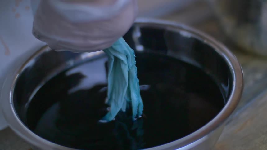 A woman removing dyed fabric from a bowl of dye