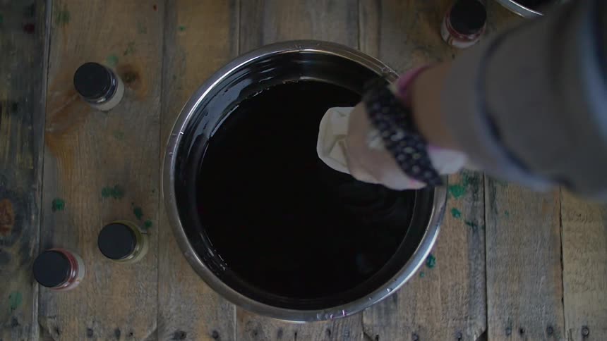 A woman dipping white fabric in a bowl of die