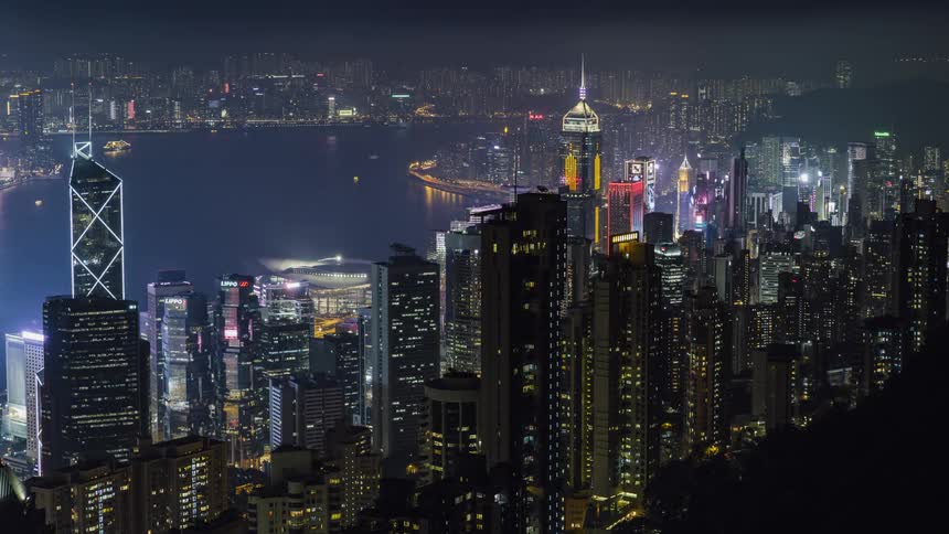Boats floating in a harbor near tall skyscrapers at night