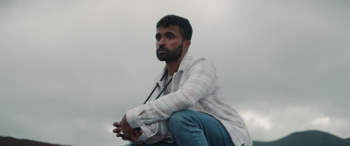 A man is outside taking photographs and there are mountains in the distance under a cloudy sky