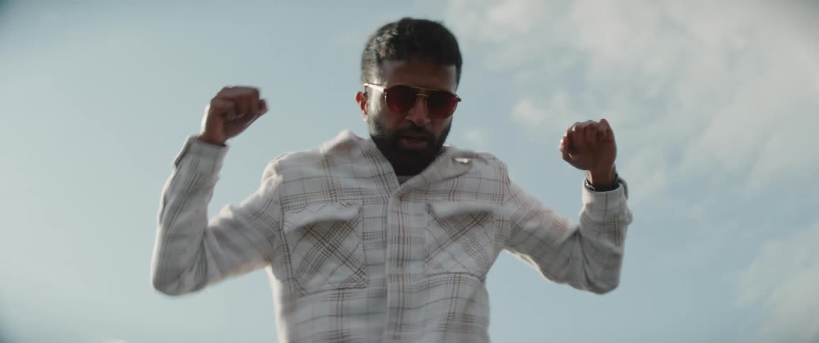 Man with a pair of brown boots jeans shirt beard and sunglasses dances in the field