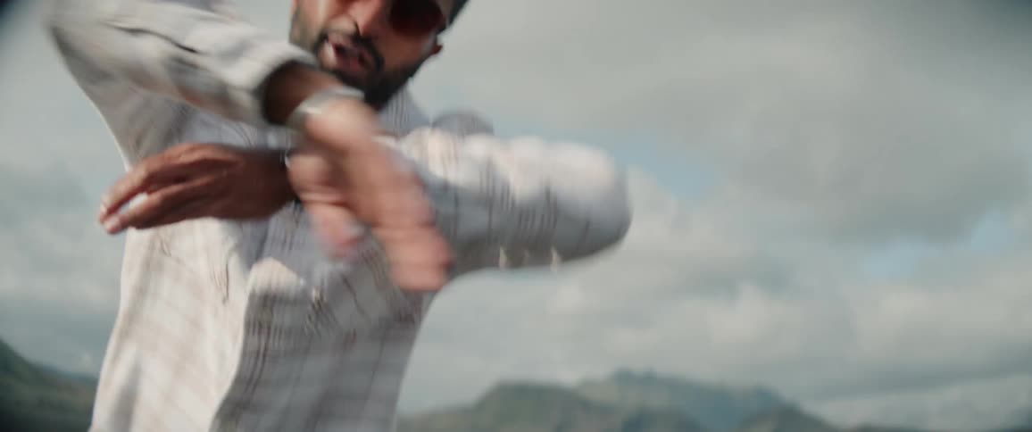 A man dances outside in a bare landscape with hills in the background