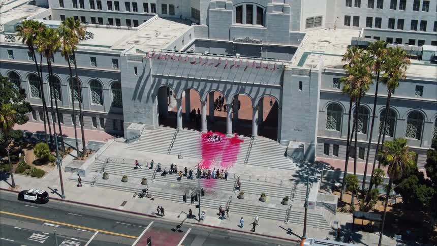 Aerial view of a crowd gathered on the entrance of a building around a stain of fuschia paint on the staircase