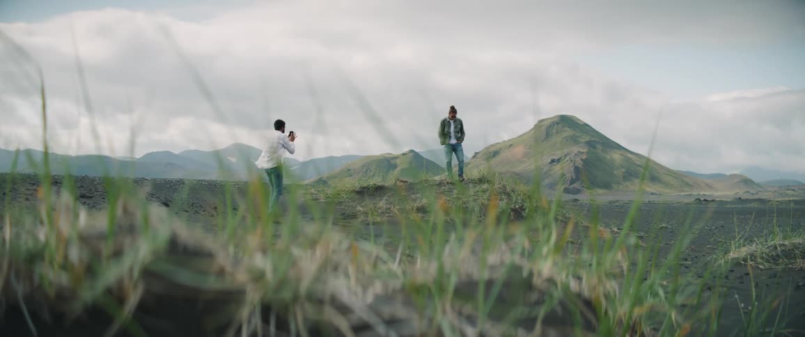 Man takes pictures of a model standing over a mound on a plain near the mountains