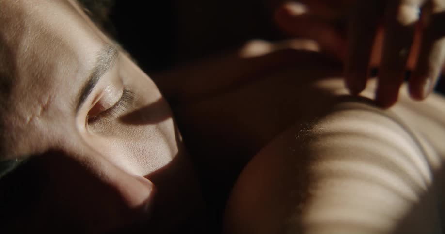 Sunlight shines on the face of a man lying on his stomach as someones fingers move across his back