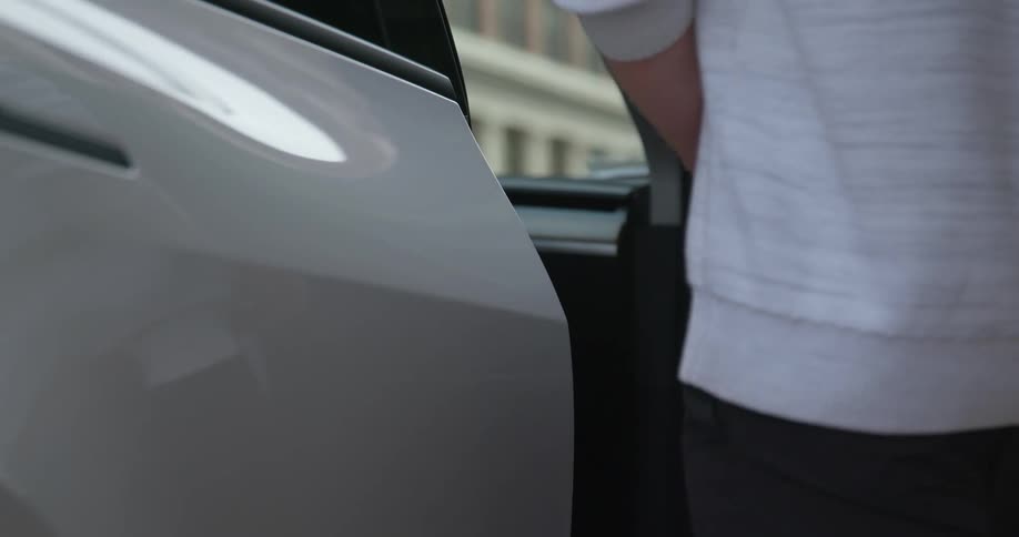 Man boarding a white parked car on a city street at morning