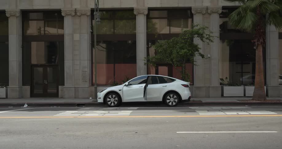 A white automobile is parked on a downtown street and two people open the doors and get inside