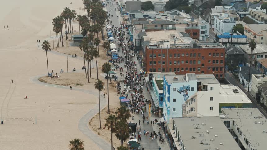 Crowds of people walk past vendors on venice beach while other bike ride and roller skate on the path