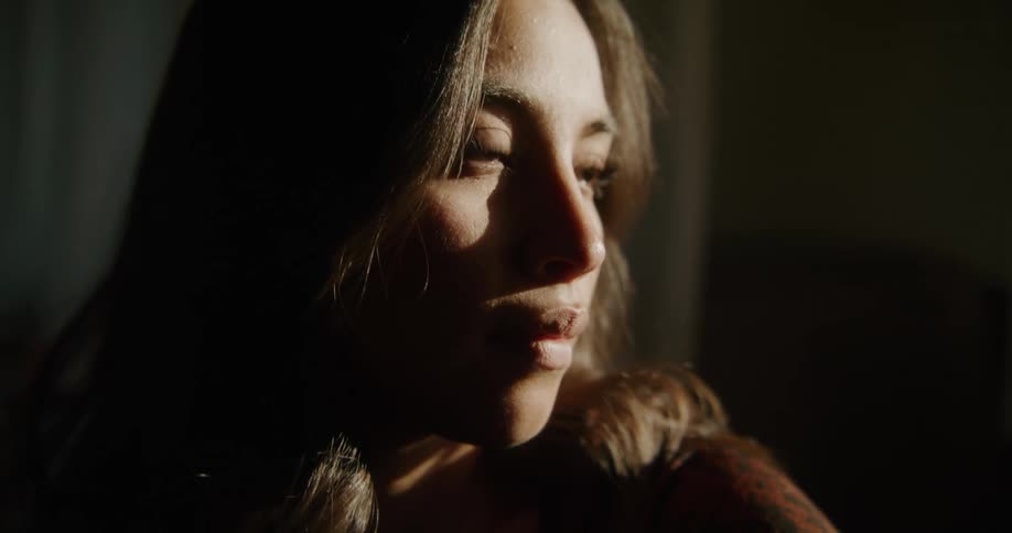 Sunlight shines on the face of a woman as she sits inside near a window
