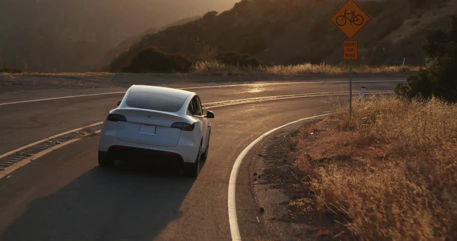 A white automobile is traveling on a road and going around a bend and there are mountains in the distance