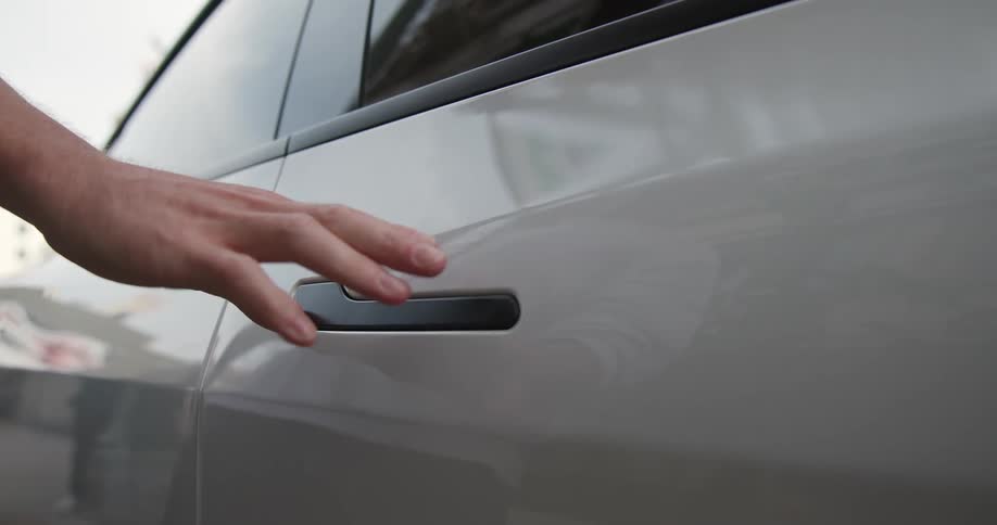 A hand is reaching out and opening the door of a white automobile