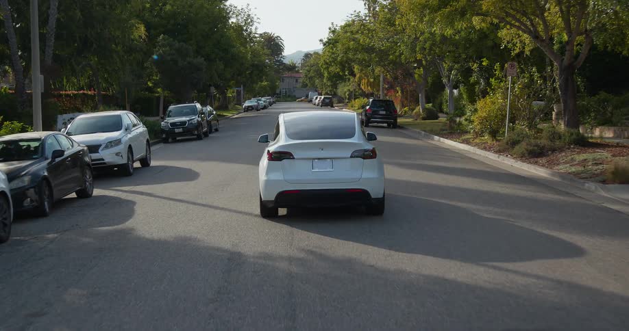 White tesla electric car driving down the road on a calm neighborhood at morning