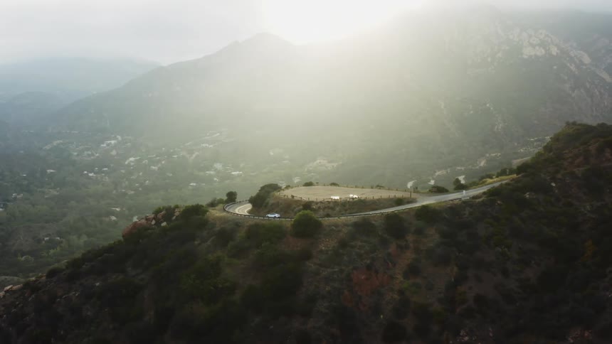 A vehicle drives down a curved road at the top of a hill