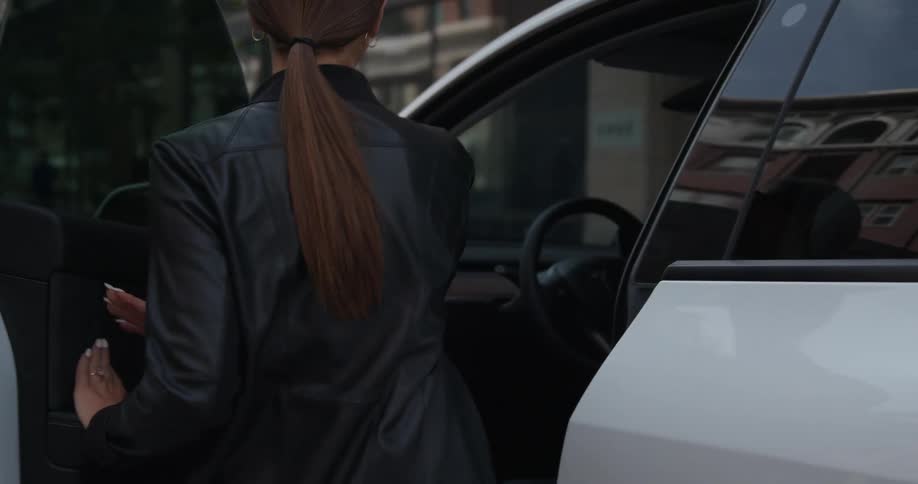 Young happy woman wearing sunglasses opens the door of a car parked on a city street at morning
