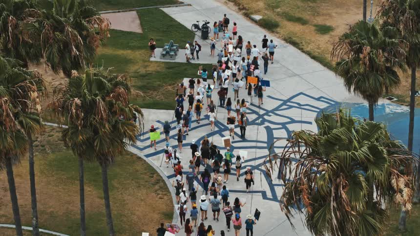 People marching in a demonstration are carrying signs as they walk through a park