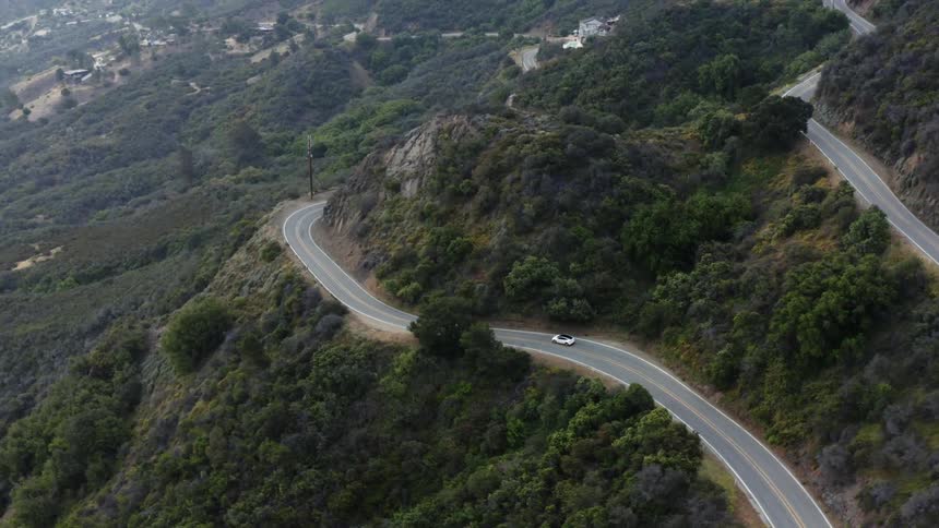 Roads wrapping around mountains as an automobile travels toward a mountainside neighborhood
