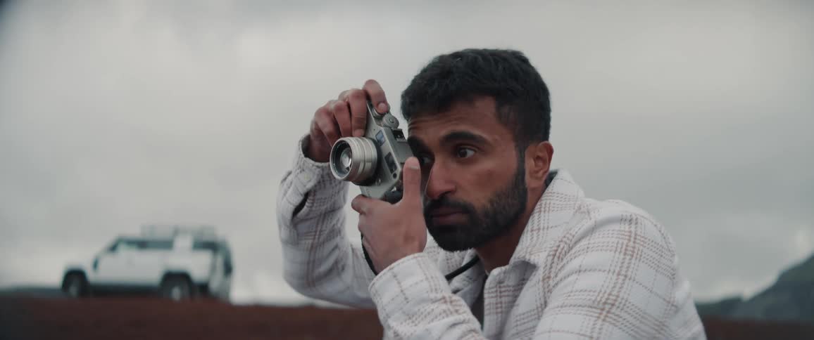 A man kneels down in a dirt field to take photos