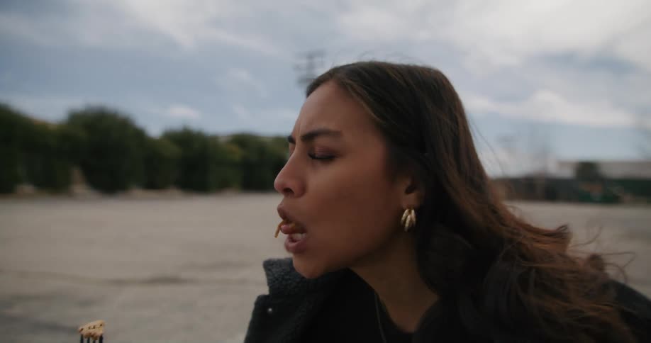 Man makes woman with wavy hair and earrings eat spagetti outdoors