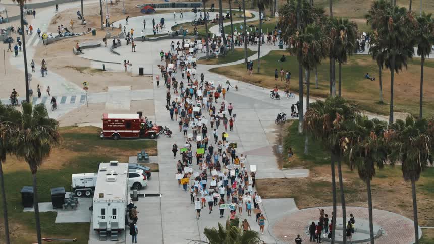 People marching in a demonstration are carrying signs as they walk through a park