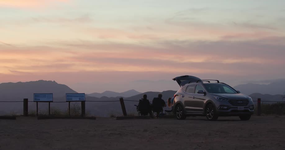 Two men sit behind a fence and watch the sun set over mountains